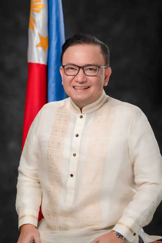 Official portrait of Raymond Alvin Garcia in a barong tagalog beside the Philippine flag